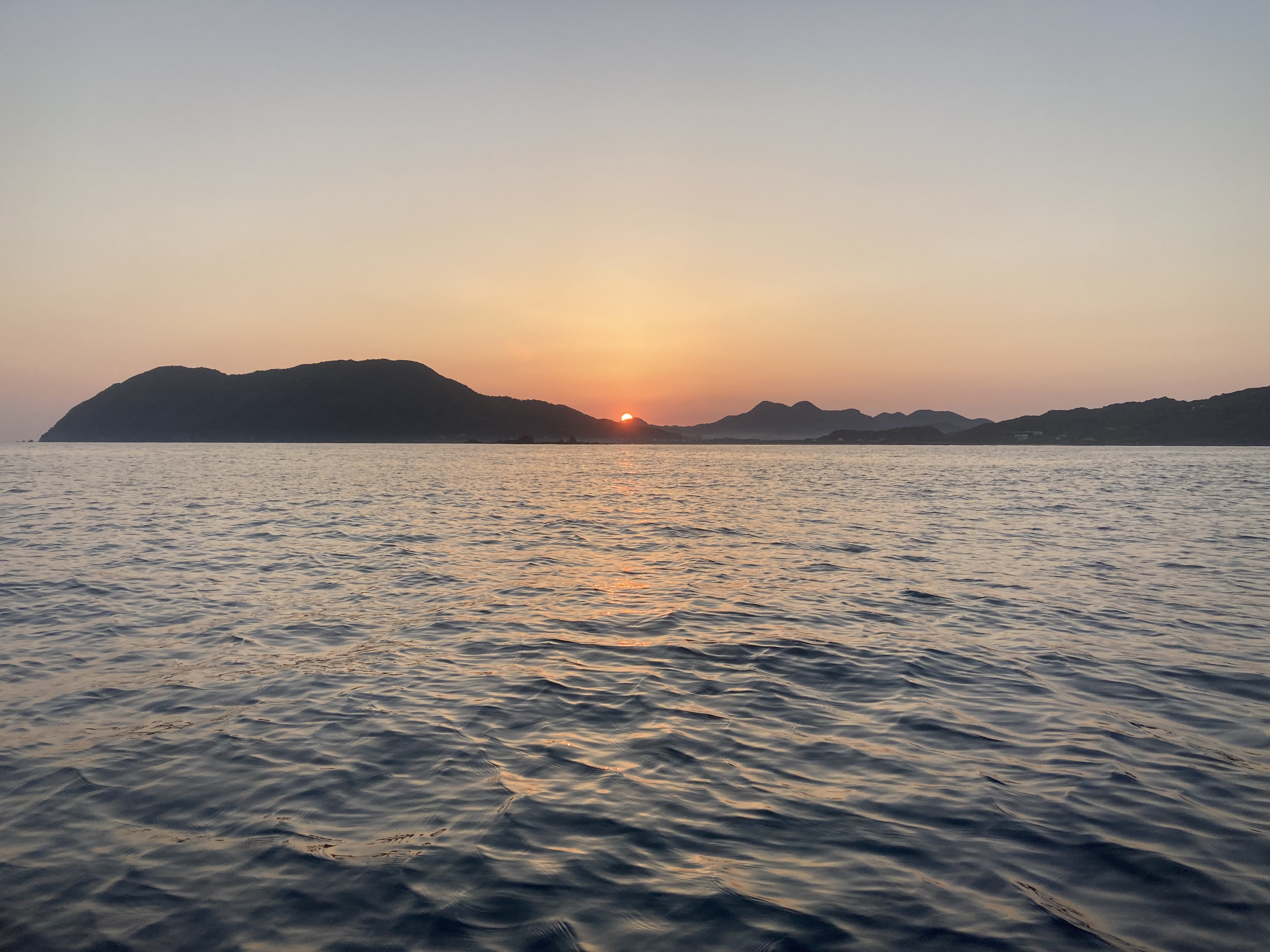 朝日が島のシルエットから昇る。穏やかな早朝の野北海岸。
